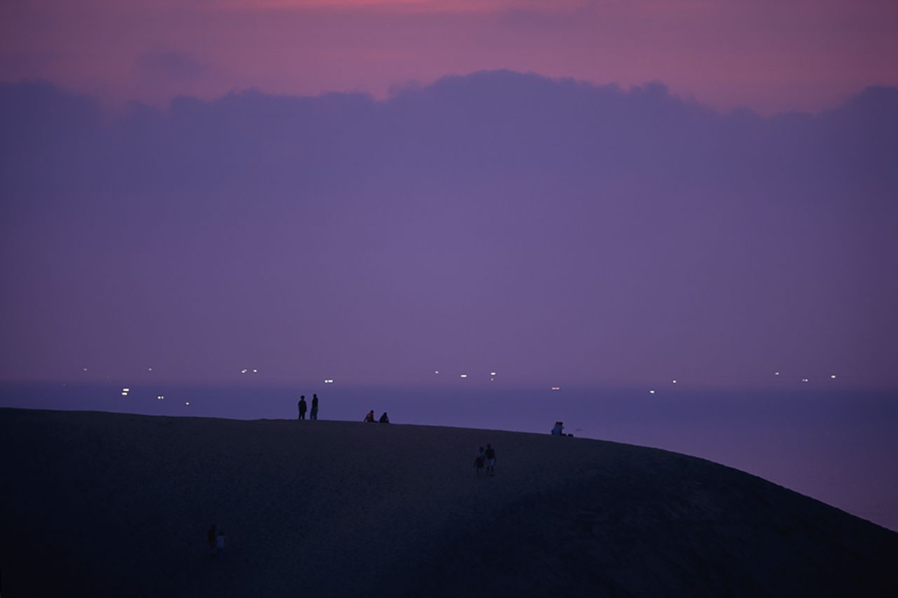 La silueta de las dunas en el atardecer, con el fondo de los isaribi, fuegos que se encienden en el mar para atraer a los peces. (Fotografía: prefectura de Tottori.) 
