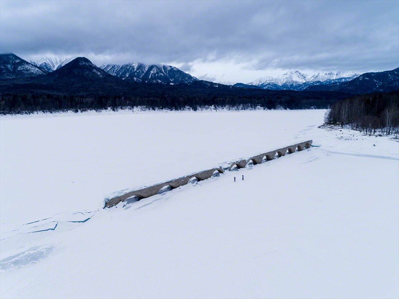 Al disminuir el nivel del pantano en enero, el puente emerge de la superficie helada del lago, rodeado por las montañas de la sierra Higashi Daisetsuzan.