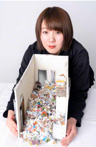 La autora con la miniatura que representa una muerte solitaria en una vivienda llena de basura.