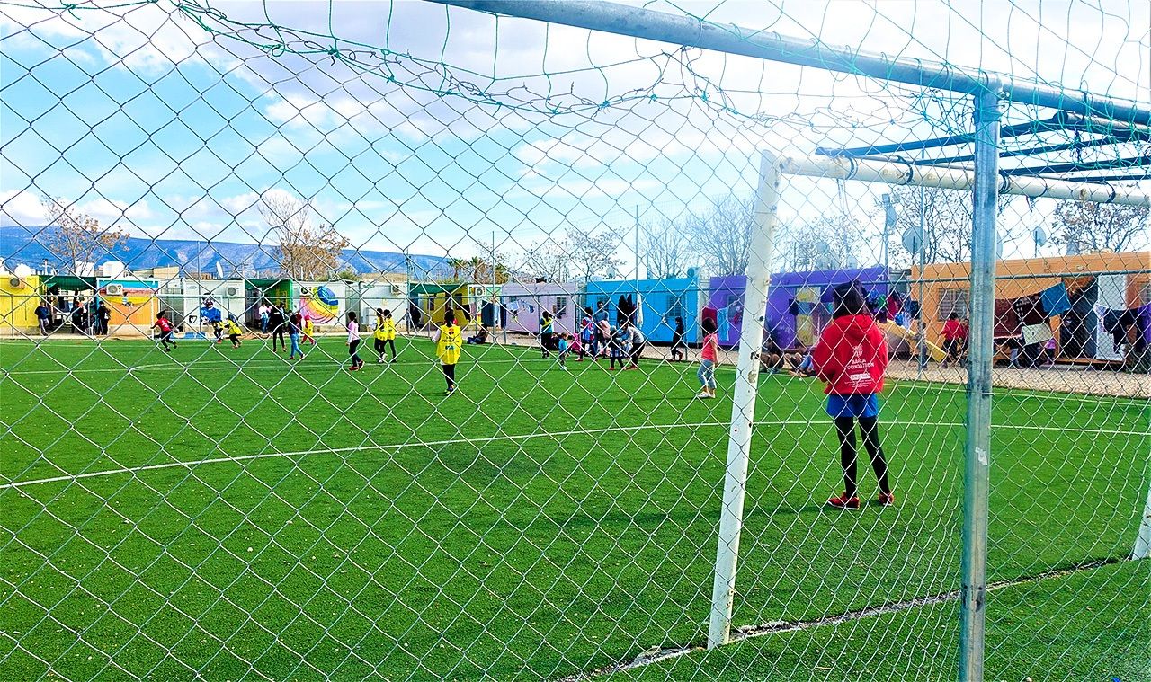 Un campo de fútbol de césped natural rodeado de coloridas viviendas provisionales (Fotografía del autor).
