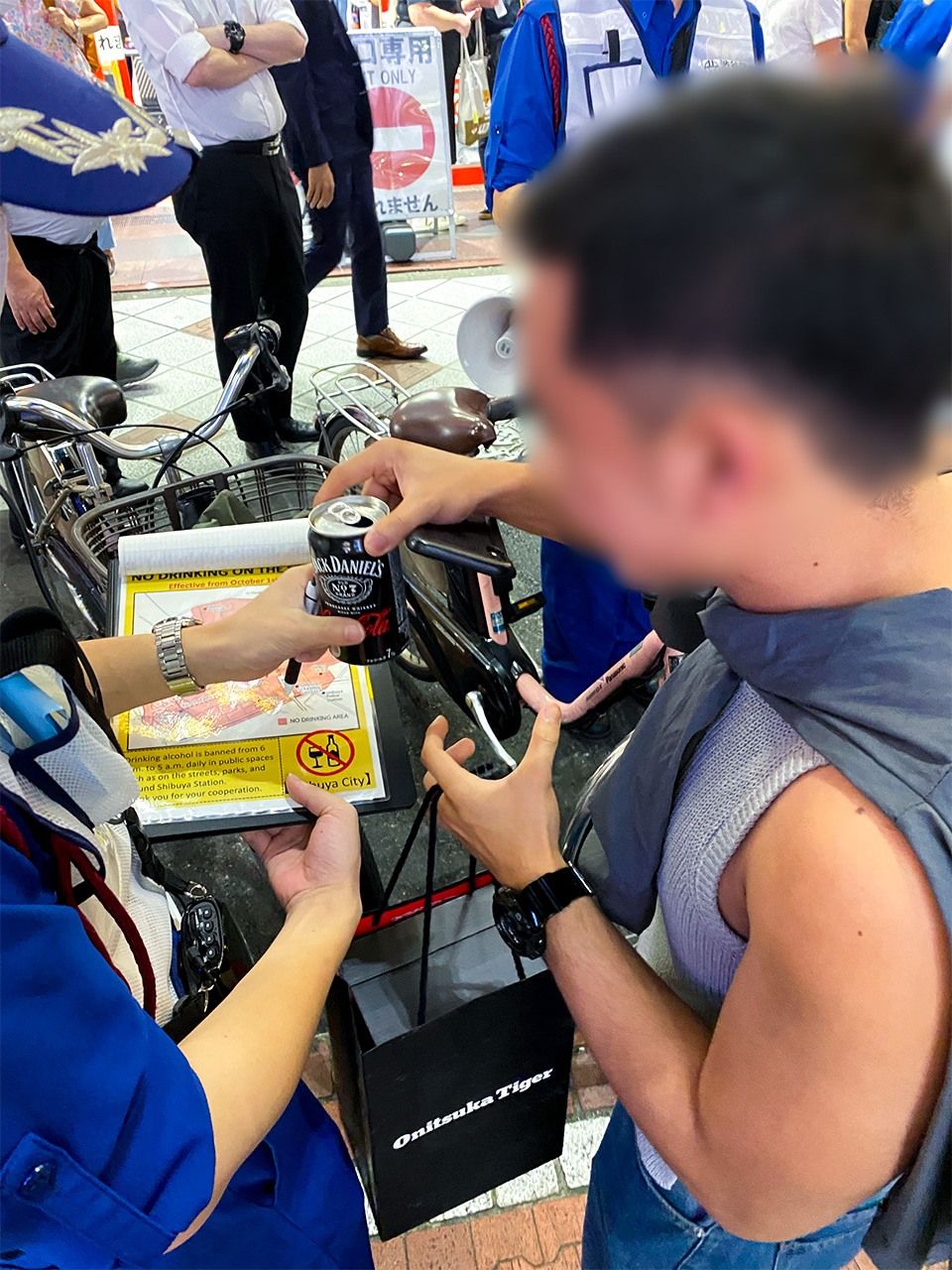 Un extranjero entrega una lata de alcohol después de escuchar las explicaciones de una patrulla cerca de la estación de Shibuya el 4 de octubre de 2024. Fotografía editada para proteger la privacidad. (© Inose Hijiri)
