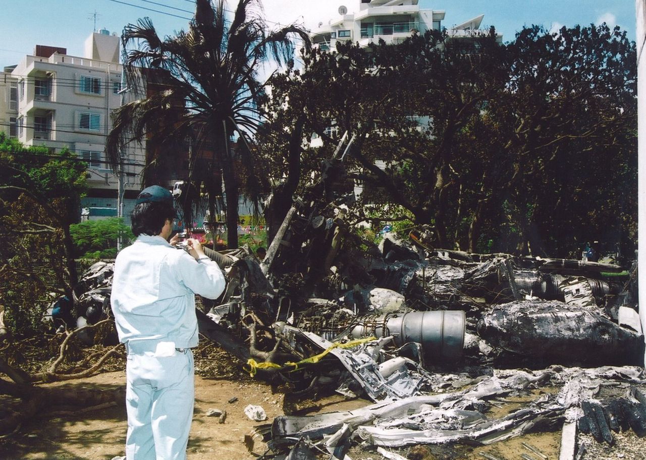 Funcionarios japoneses examinan los restos de un helicóptero militar estadounidense esparcidos cerca de la pared sur del edificio principal de la Universidad Internacional de Okinawa en el campus de la universidad en Ginowan, 15 de agosto de 2004. (Jiji Press)