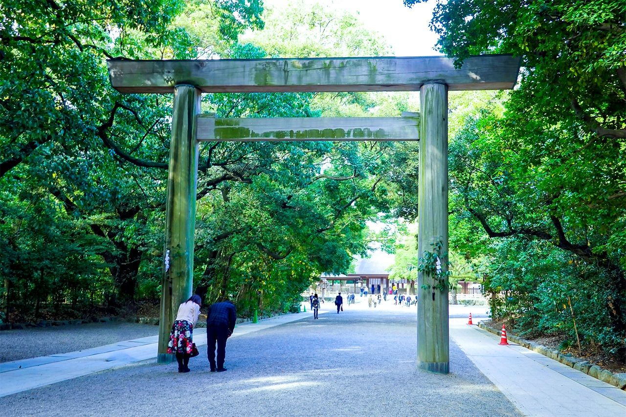 Visitantes haciendo una reverencia antes de pasar bajo un torii (© tenjou/Pixta)
