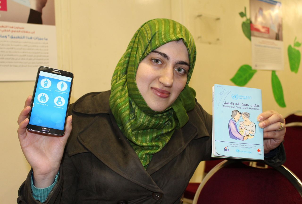 Rawan Hussein, una mujer palestina que vive en un campo de refugiados, sostiene un teléfono con la aplicación de boshi techō y la versión en papel del manual. (Imagen tomada el 4 de abril de 2017 en el centro sanitario de la Agencia de Naciones Unidas para los Refugiados de Palestina en Oriente Próximo, situada en Ammán, Jordania). Los refugiados llaman al manual pasaporte de vida. (Jiji Press)
