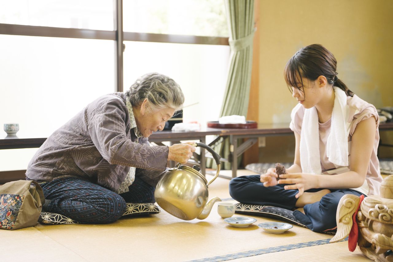 Hanae (izquierda) expresa sus sentimientos hacia la familia por medio de su contacto con Ayaka. La actriz que la interpretaba, Sasaki Sumie, murió a los 90 años, en febrero de 2019, sin llegar a ver la película terminada © Comité de Producción de Momi no ie.