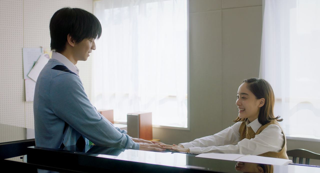 Satoshi disfruta escuchando a Masuda Manami (Yoshida Mikako), una compañera de clase en la escuela para ciegos, que toca el piano. ©Throne / Karavan Pictures