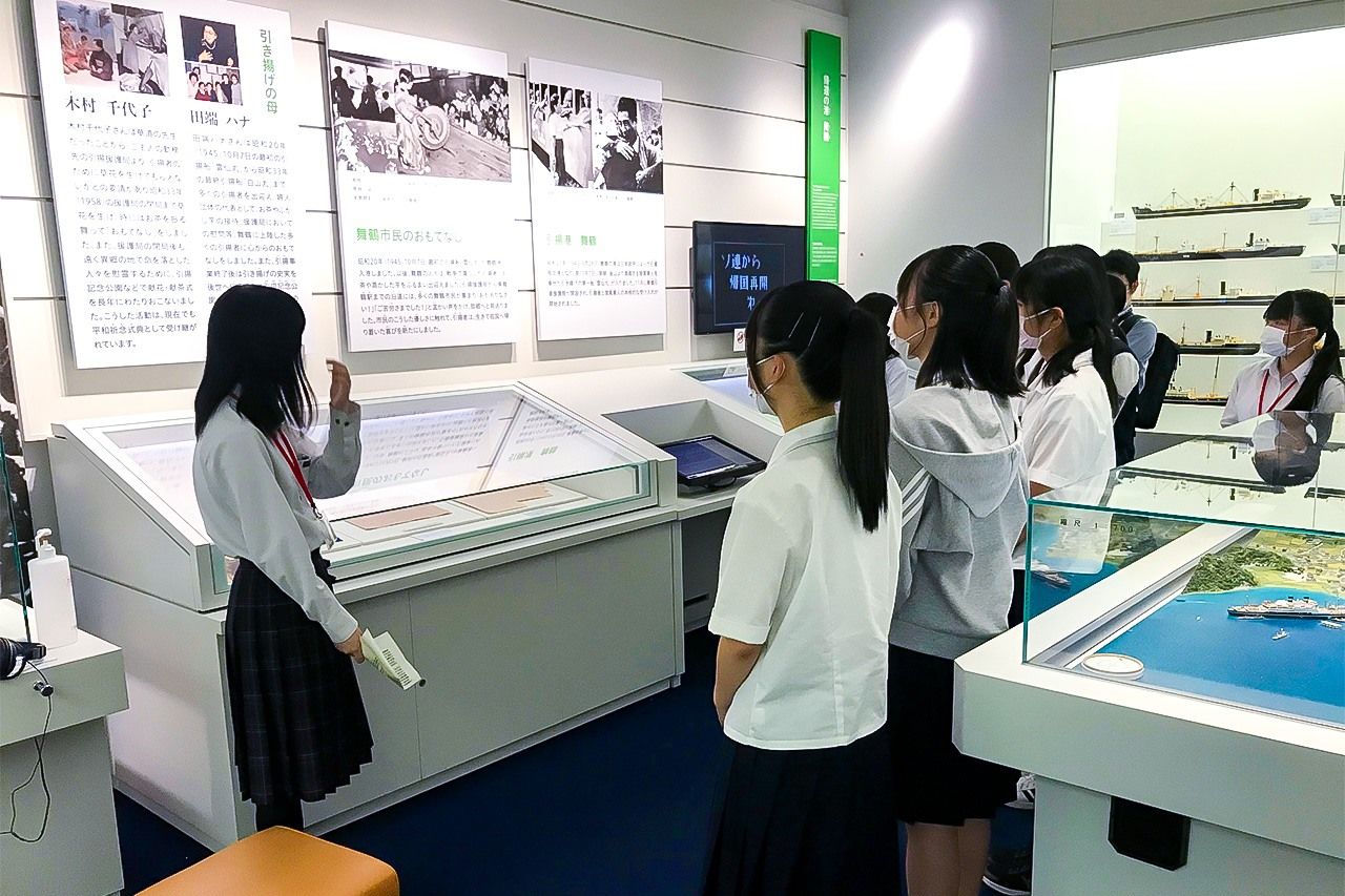 Una integrante del círculo de narradores explica la exposición del Museo Conmemorativo de la Repatriación de Maizuru a un grupo de visitantes de su misma edad. (Museo Conmemorativo de la Repatriación de Maizuru)