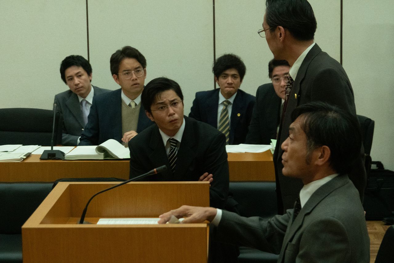 El teniente inspector Kitamura (Watanabe Ikkei, abajo a la derecha) de la Oficina de Prevención de Delitos Tecnológicos de la Policía Prefectural de Kioto, el agente que interrogó a Kaneko tras su detención, presta declaración ante el tribunal. ©2023 Comité de producción de Winny