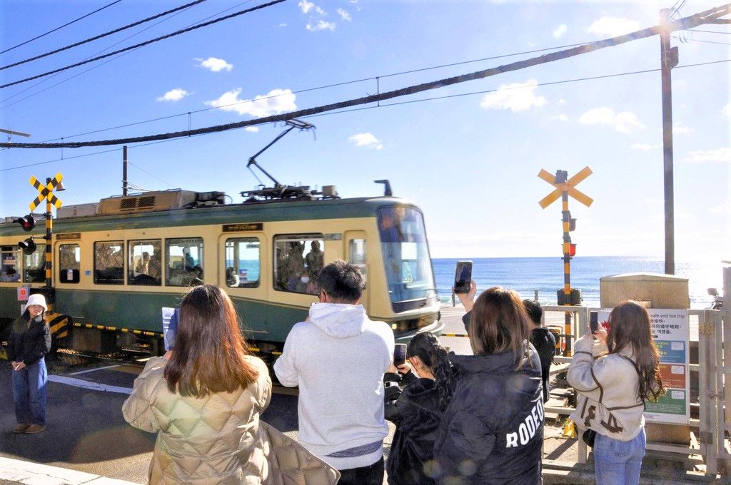 Aficionados visitando el paso a nivel del Ferrocarril Eléctrico de Enoshima representado en Slam Dunk. Independientemente de la nacionalidad, continúan las peregrinaciones a localizaciones veneradas por las personas fascinadas con la obra. (Kamakura, prefectura de Kanagawa, diciembre de 2022)