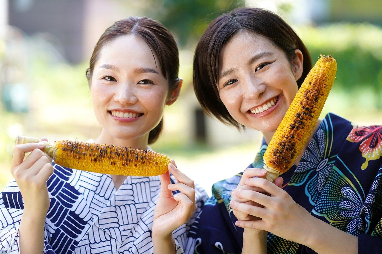 Dos chicas comiendo maíz asado. (PIXTA)