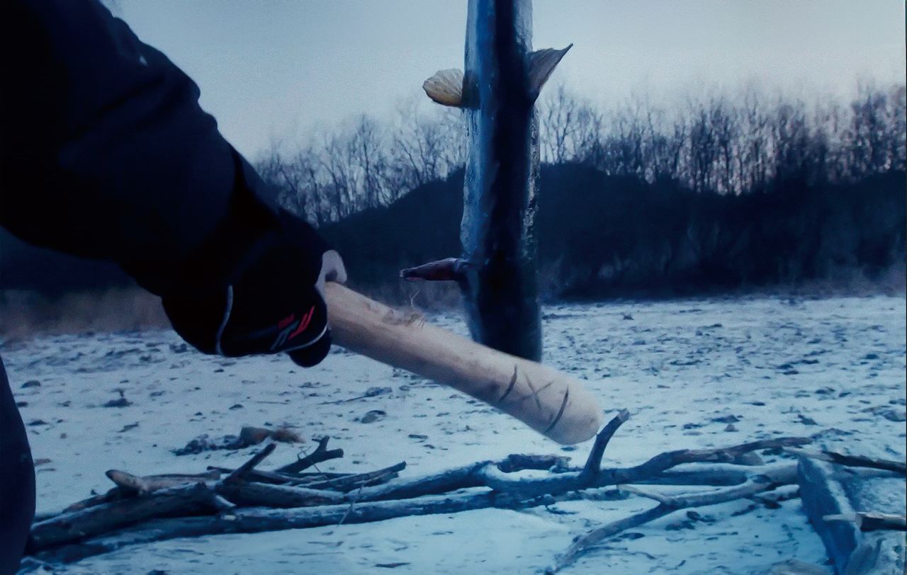 Shige golpea la cabeza del salmón con un ipakikni para matarlo. (© 2024 Takeshi Fukunaga/AINU PURI Production Committee)