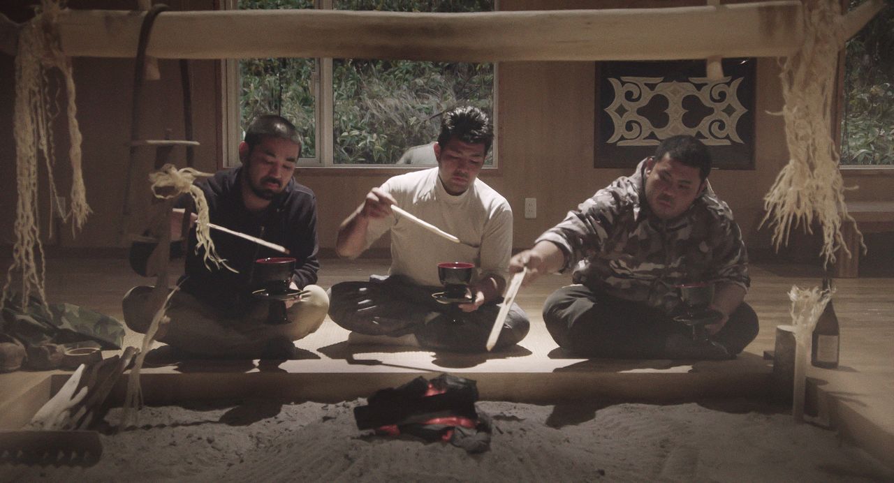 Shige, su amigo Satoshi y Ryūtarō informan a los dioses de que han elaborado un inaw para ofrendarlo en el lugar de la pesca. (© 2024 Takeshi Fukunaga/AINU PURI Production Committee)