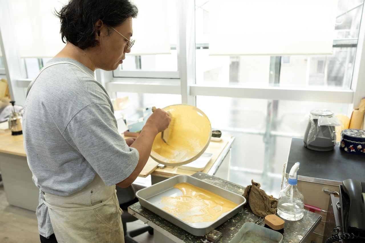 Takasugi extiende la pintura preparada sobre un tamiz cubierto con una tela.