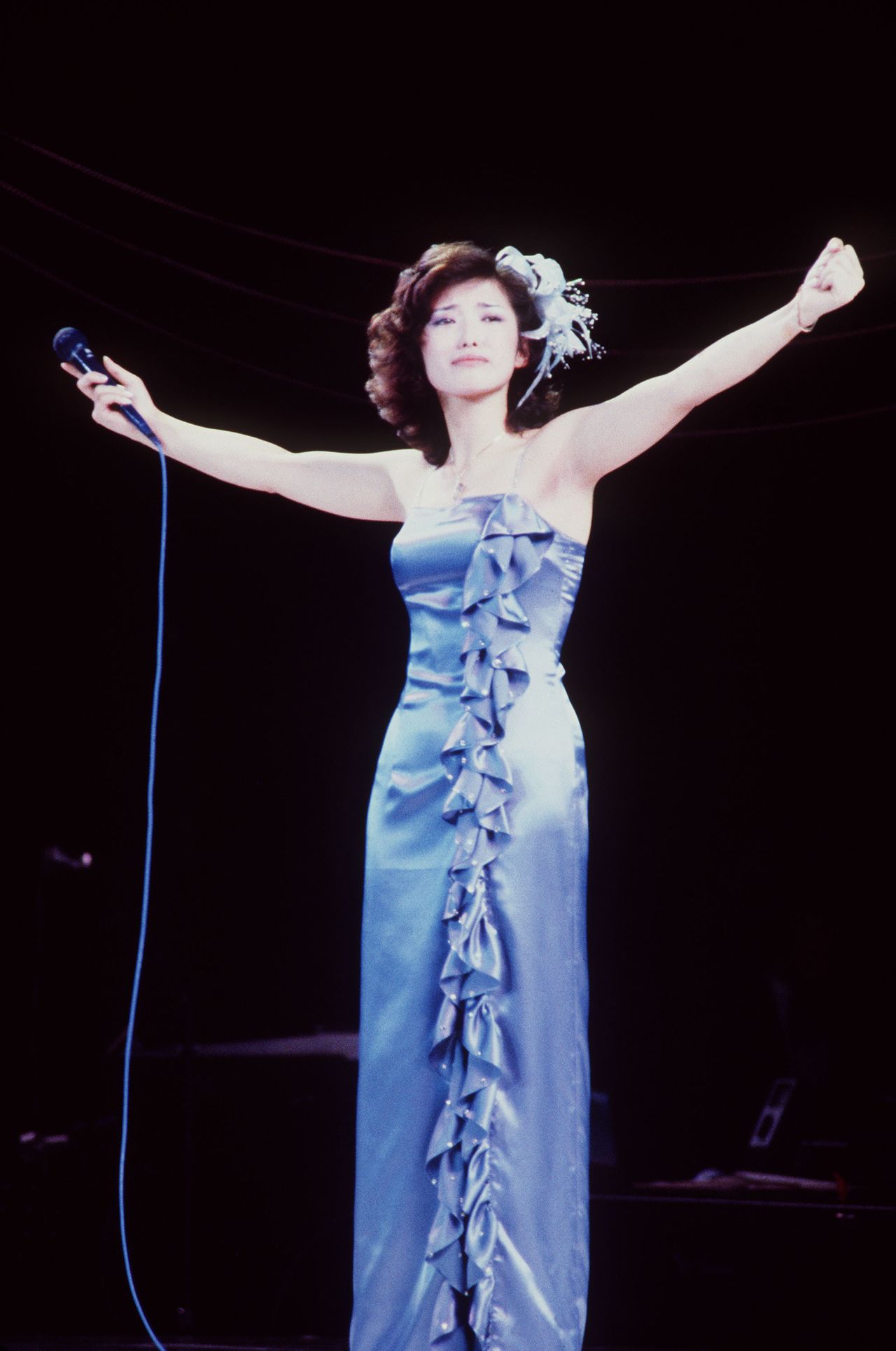 El 5 de octubre de 1980 la popular cantante Yamaguchi Momoe puso un punto final a su carrera con un concierto de despedida en el Nippon Budōkan. Al terminar de cantar Sayonara no Mukōgawa, la canción interpretada en el bis, dejó silenciosamente el micrófono sobre el escenario. Tras su participación en el programa de audiciones Star Tanjō (“El nacimiento de una estrella”), debutó como cantante en 1973. Junto con Mori Masako y Sakurada Junko, lideró el auge de las idols en la década de 1970. En marzo de 1980, al anunciar su compromiso con el actor Miura Tomokazu, declaró que abandonaría el mundo del espectáculo. En los ocho años transcurridos desde su debut, dejó numerosos éxitos como Hitonatsu no keiken, Imitation Gold, Playback Part 2, Kosumos e Ii hi tabidachi. Yamaguchi Momoe en su concierto de despedida. (Jiji)