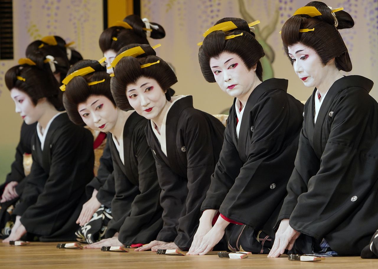 Mujeres vestidas con kimono negro de manga corta con mon y cuello blanco, con el pelo recogido al estilo Shimada-mage, como dictaba el reglamento de indumentaria para las geishas. La imagen corresponde al ensayo de la víspera del Azuma Odori, un recital que se representa en el Shinbashi Enbujō, un teatro que se fundó para exhibir los resultados de las prácticas de música y danza de las geishas de Shinbashi. (Mayo de 2019, Jiji Press.)