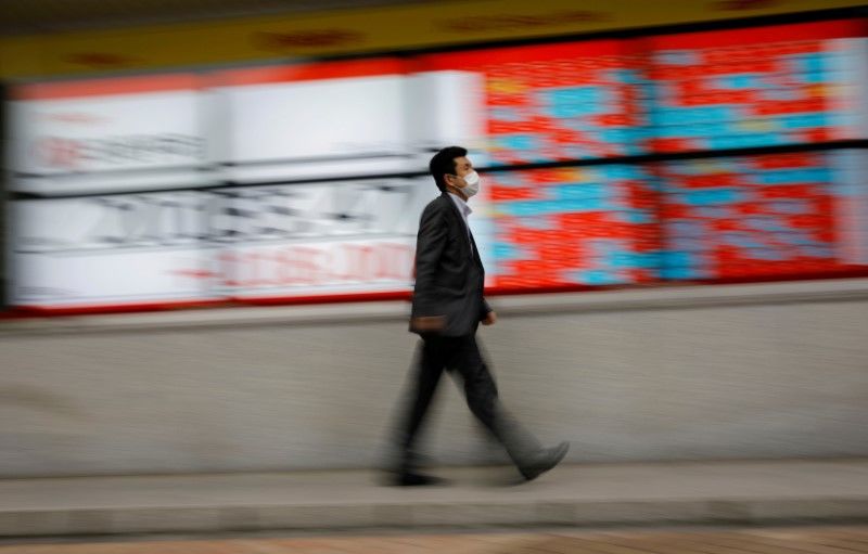 FILE PHOTO: A man wearing a protective face mask, following the coronavirus disease (COVID-19) outbreak, walks in front of a stock quotation board outside a brokerage in Tokyo, Japan, May 18, 2020. REUTERS/Kim Kyung-Hoon/File Photo