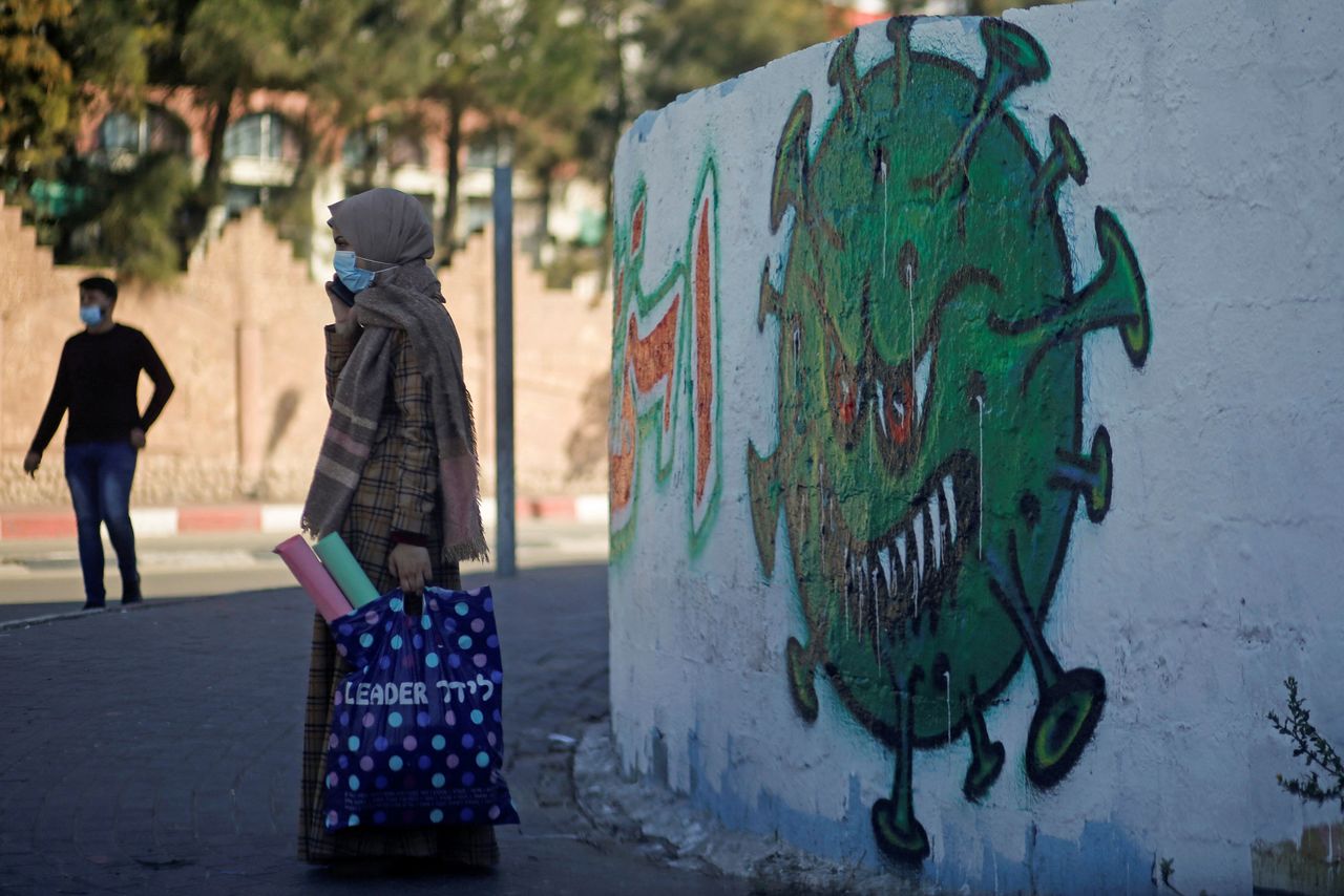 FOTO DE ARCHIVO: Una mujer con mascarilla habla por teléfono frente a una caricatura de un coronavirus en Gaza, el 22 de noviembre de 2020. REUTERS/Mohammed Salem