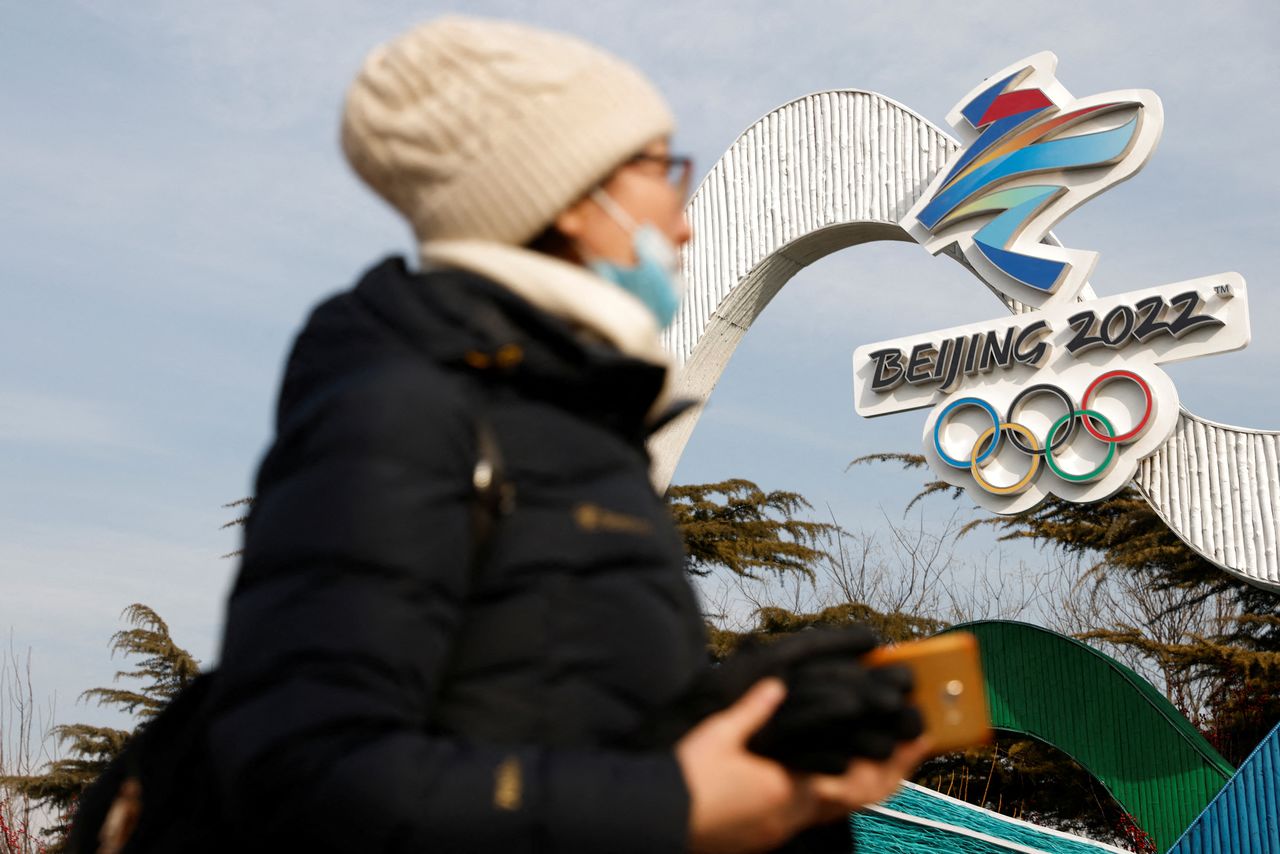 Una mujer con mascarilla pasa frente al logotipo de los Juegos Olímpicos de Invierno 2022 en una instalación en Pekín, China, el 18 de enero de 2022. REUTERS/Carlos Garcia Rawlins