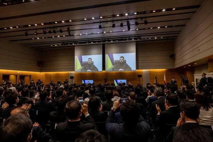Miembros de la Cámara baja del Parlamento japonés aplauden mientras la imagen del presidente ucraniano, Volodímir Zelenski, aparece en una pantalla a través de enlace de video en el edificio de la Cámara de Representes en Tokio, Japón. 23 marzo 2022. Behrouz Mehri/Pool vía Reuters