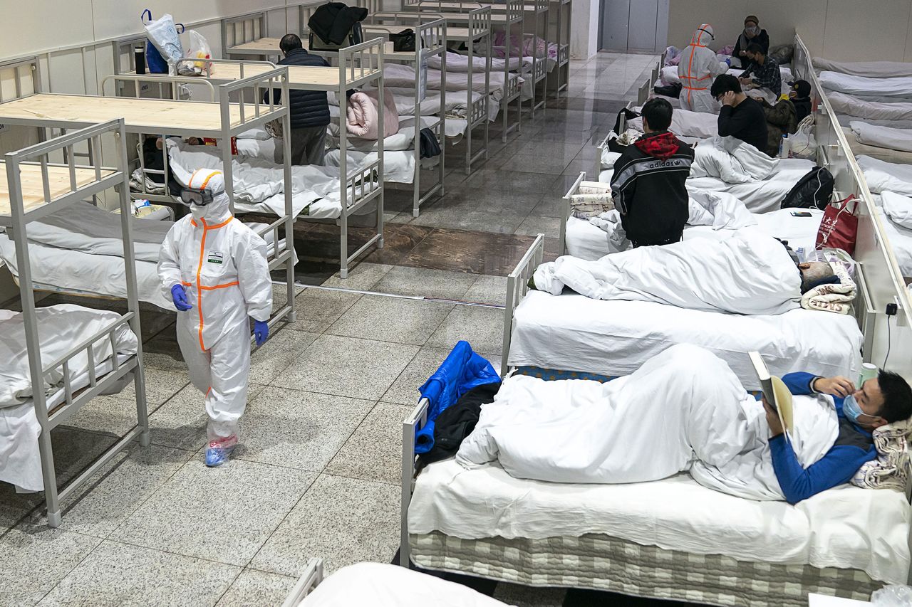 Un médico con traje de protección pasa entre pacientes del coronavirus acomodados en las camas de un hospital improvisado en un centro de exposiciones de la ciudad china de Wuhan, el 5 de febrero de 2020. (Chinatopix/AP/Aflo)