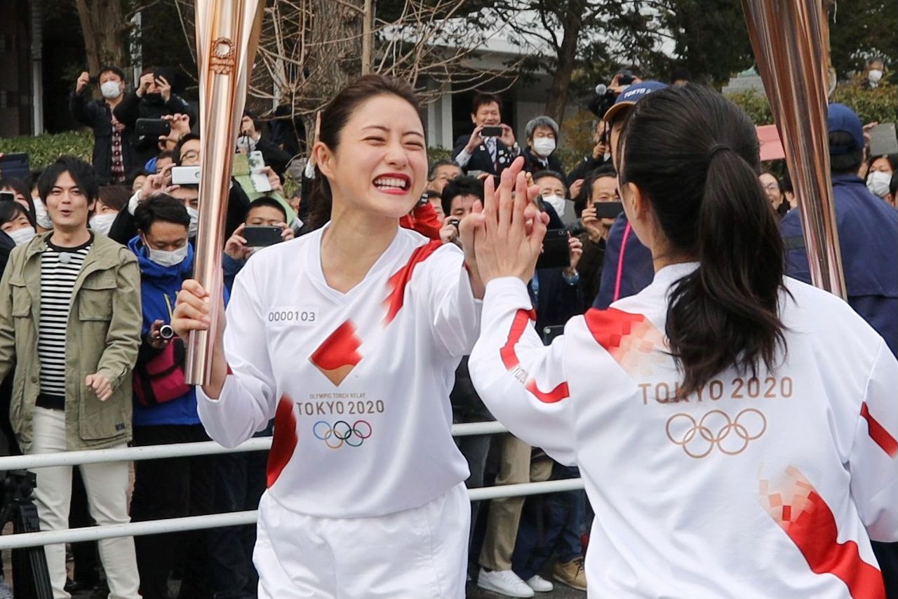 La actriz Ishihara Satomi (a la izquierda) “choca los cinco” con la siguiente corredora durante el ensayo del relevo de la antorcha de los Juegos Olímpicos de Tokio el 15 de febrero de 2020. (© Jiji)