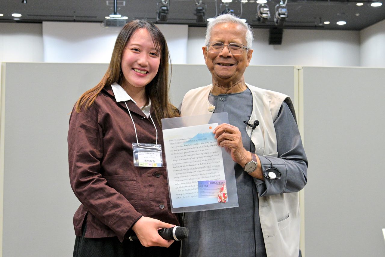 Muhammad Yunus (a la derecha) recibe un mensaje de una participante joven en el acto celebrado el 25 de marzo de 2026. (© Fundación Sasakawa para la Paz)