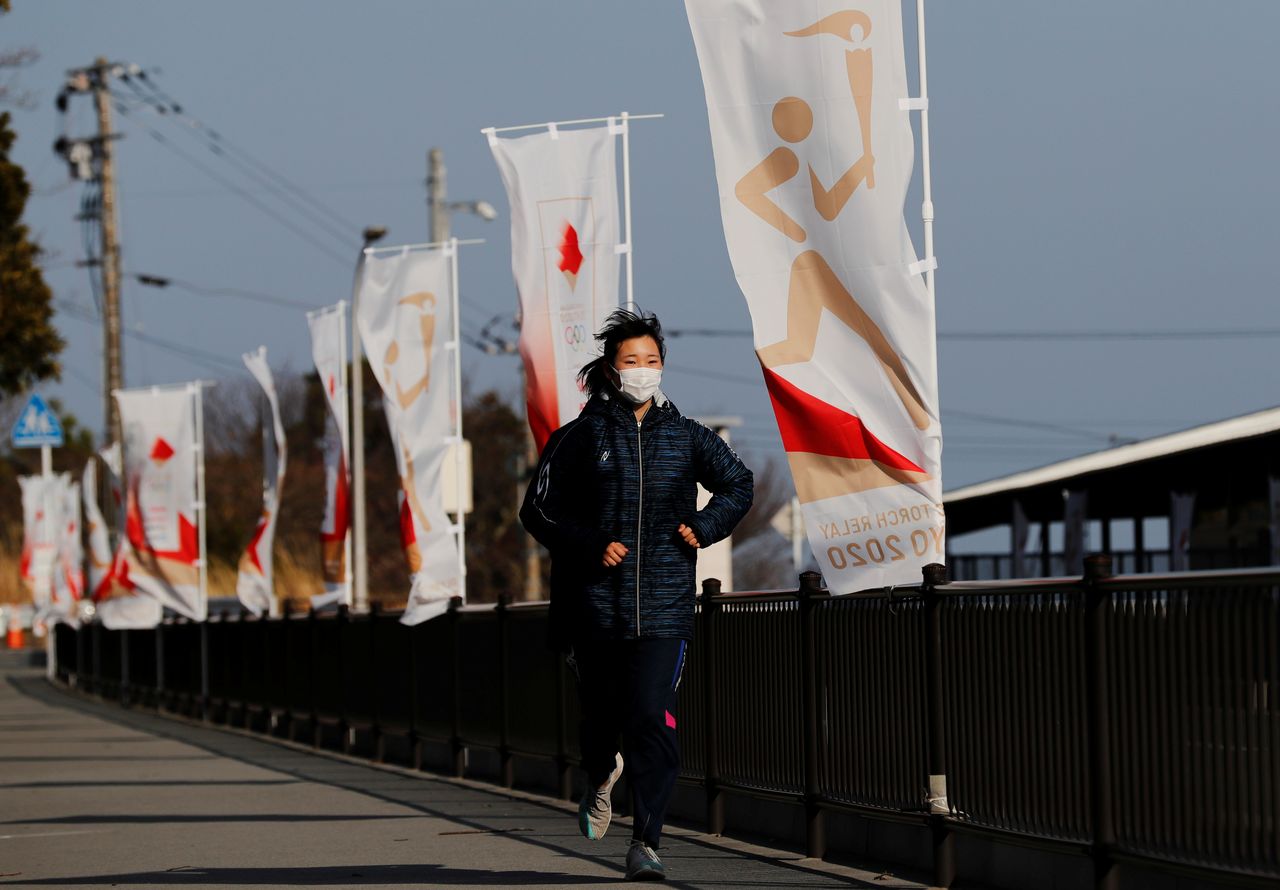 La estudiante de secundaria Rena Arakawa, quien portará la antorcha olímpica en el primer día de su relevo por los Juegos Olímpicos de Tokio 2020, corre junto a unas banderas que promeven el recorrido durante una entrevista con Reuters en Hirono, prefectura de Fukushima, Japón. 4 de marzo, 2021. REUTERS/Kim Kyung-Hoon
