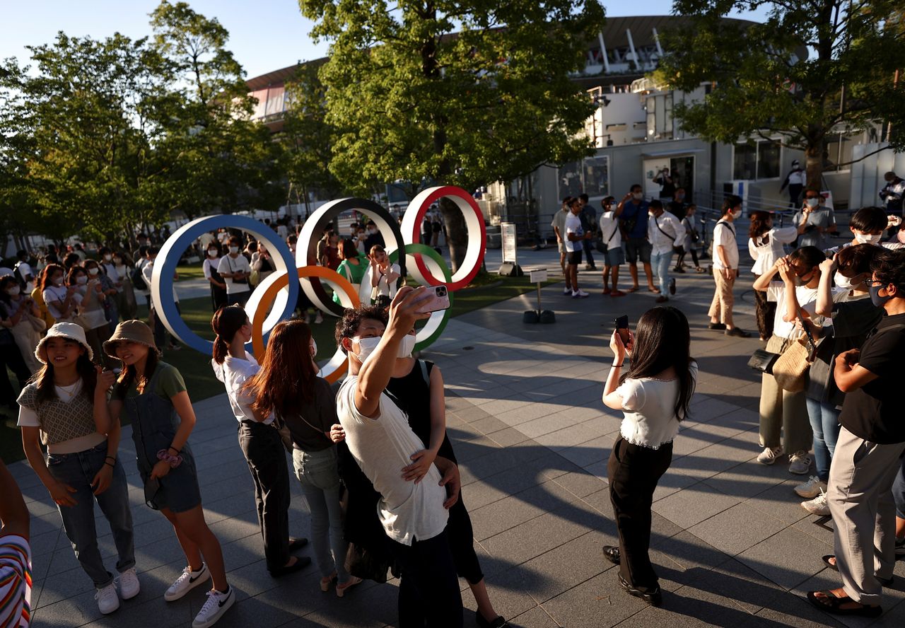 Foto del sábade de un grupo de personas sacándose fotos junto a los anillos olímpicos fuera del Estadio Nacional de Tokio. 
Jul 31, 2021.  REUTERS/Issei Kato