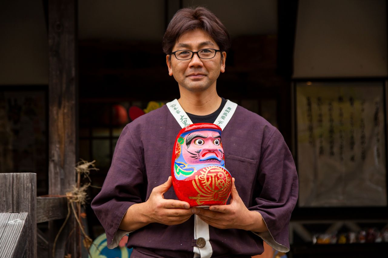 Hashimoto Shôichi tenant une poupée daruma fabriquée de ses mains.