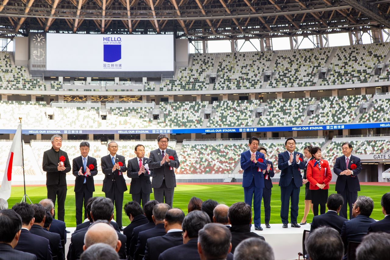 Le Premier ministre M. Abe Shinzô, le ministre chargée des Jeux olympiques Mme Hashimoto Seiko, la gouverneur de Tokyo Mme Koike Yuriko, étaient présents à la cérémonie d’achèvement des travaux. À l’extrême gauche, M. Kuma Kengo, architecte du Stade National.