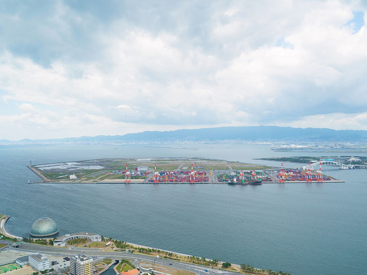 Yumeshima, qui accueillera l’Expo 2025. En juin 2019, seul signe d’activité : la présence de quelques conteneurs d'expédition. En arrière-plan, au-delà du pont, Maishima.