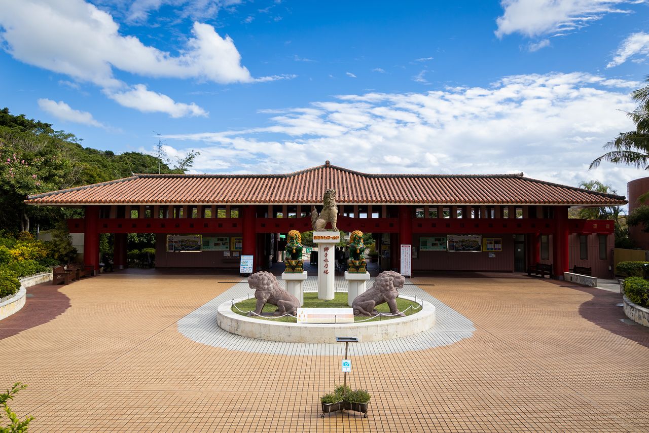 L’entrée du parc Okinawa World est un bâtiment recouvert d’un toit traditionnel en briques rouges. Devant la structure se dresse le monument appelé Shishiku-no-Tô, qui arbore fièrement l’emblème de l’île, la créature gardienne shīsā.
