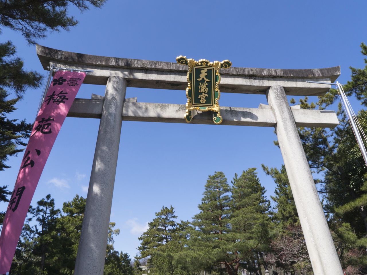 Une banderole verticale à gauche sur le portique torii annonce que les pruniers sont en fleurs au sanctuaire Kitano Tenmangû.