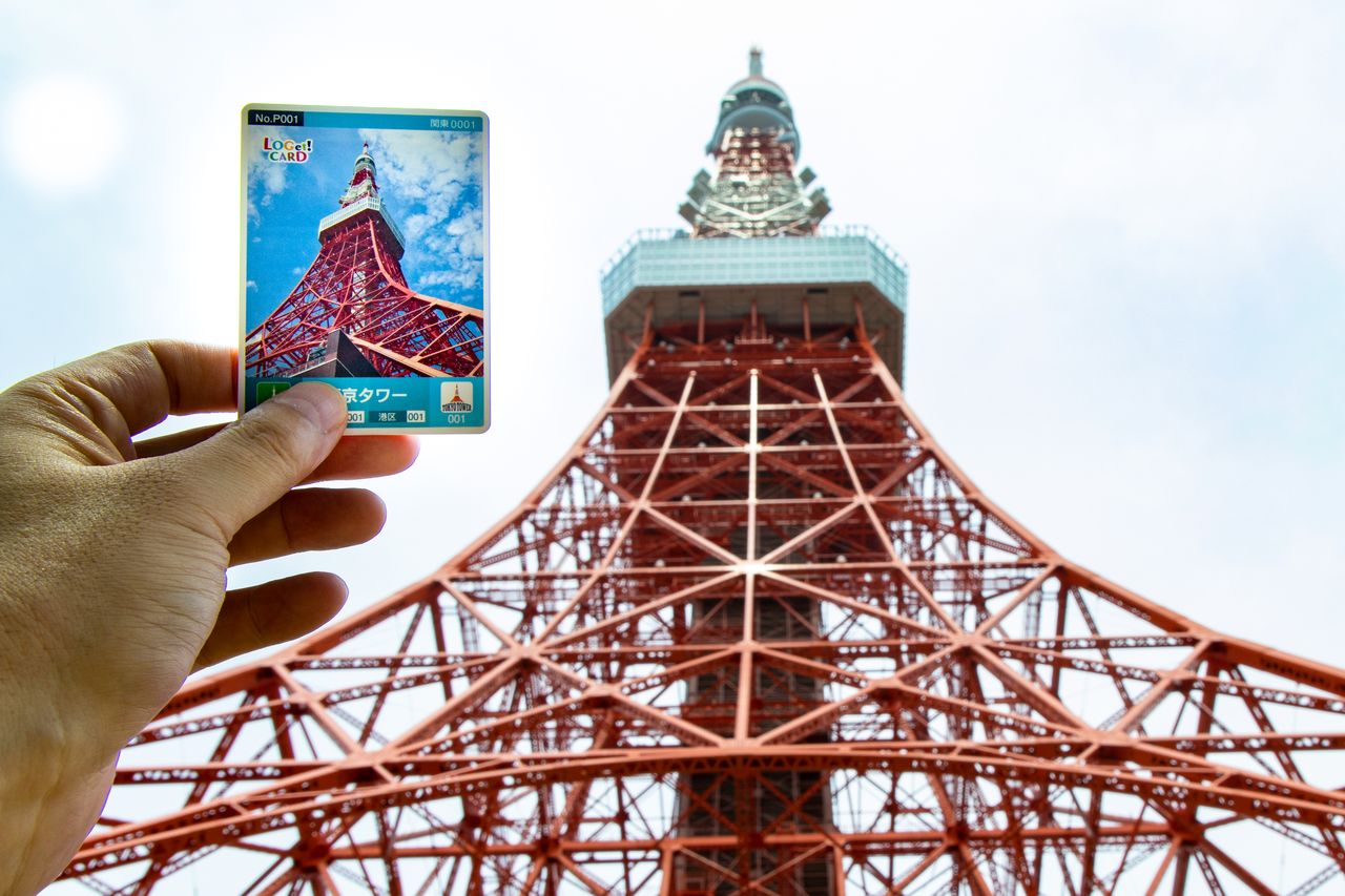 Yamada tient une carte LOGet devant l’attraction correspondante (la tour de Tokyo).