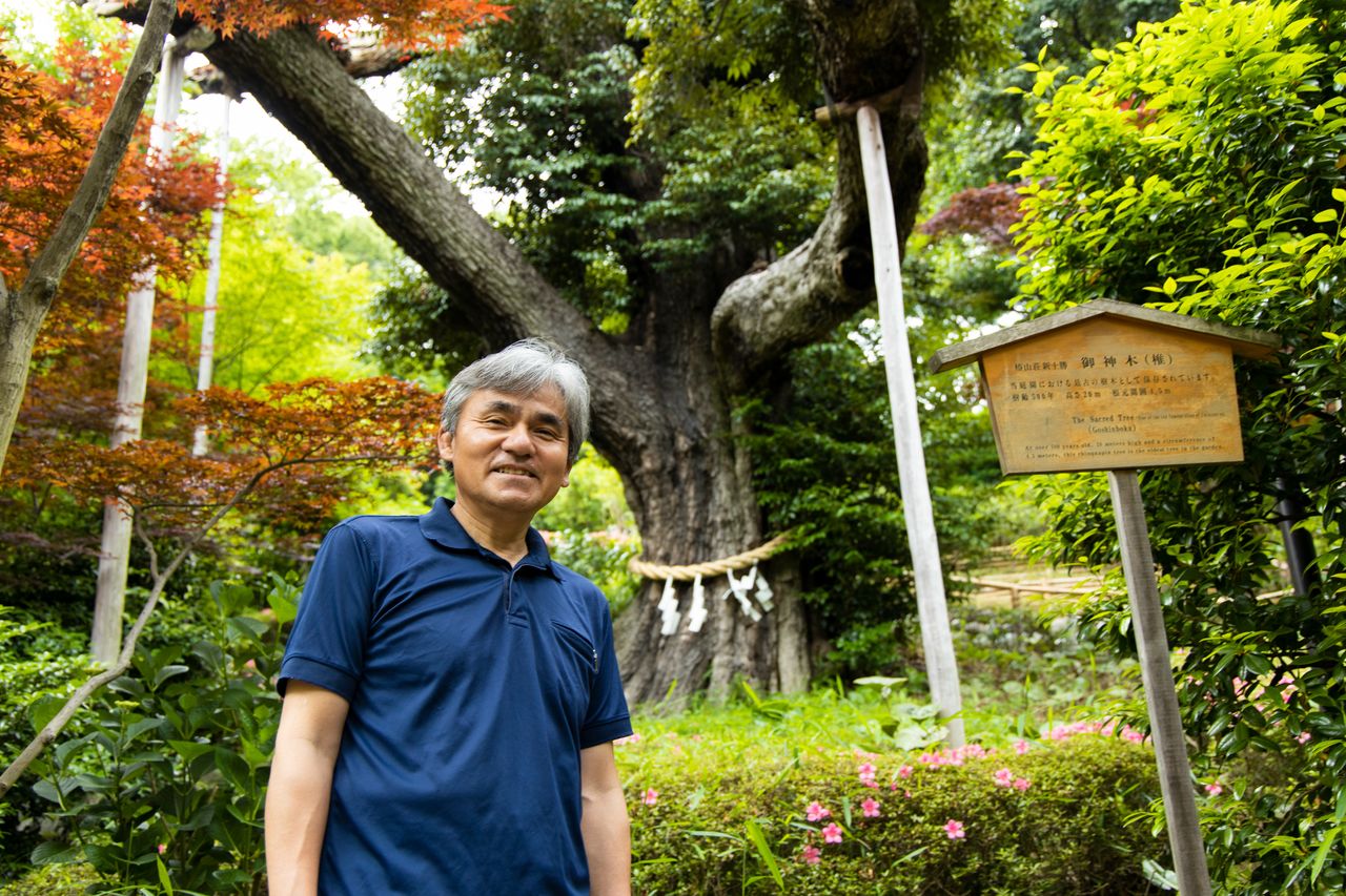 Okayasu Akira, posant devant un arbre sacré de plus de 500 ans et heureusement épargné par la guerre.