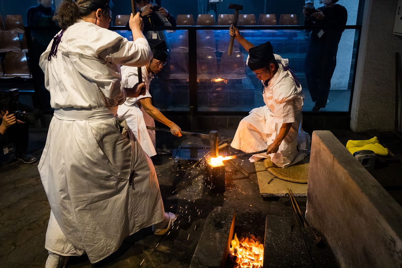 Le yokoza (à droite) donne le rythme du martelage avec un petit marteau, que les deux autres artisans suivent avec des marteaux plus volumineux.
