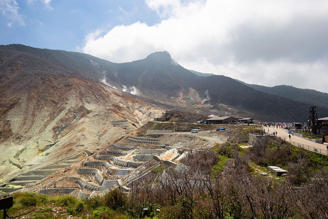 La vallée d’Ôwakudani et ses fumerolles, avec en arrière-plan le mont Kanmurigatake, haut de 1409 mètres. À Ôwakusawa, au premier plan à gauche, où les glissements de terrain sont fréquents, ont été installées des structures visant à limiter l’érosion.