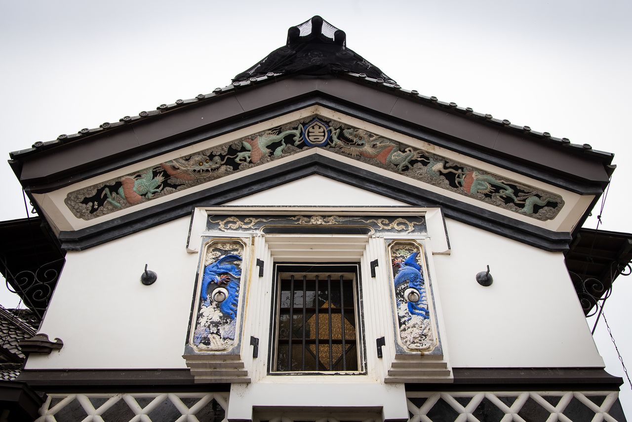 La façade du côté est de l’entrepôt après la restauration, avec les koto-e représentant des animaux réels et imaginaires, ainsi que différentes variétés de plantes. L‘original est l’œuvre du maître plâtrier Kawakami Ikichi, un grand ami de Yoshizawa Nitarô, qui partageait son sens artistique.