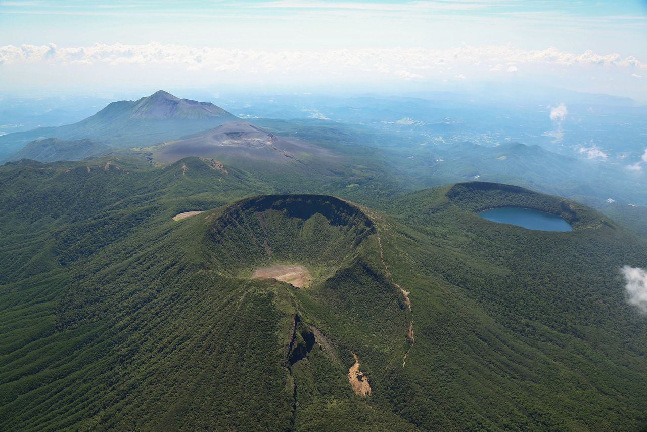 Le mont Karakuni (au premier plan) est le plus haut pic de la chaîne de montagne de Kirishima. À droite, on trouve le lac de la caldeira d’Ônami-no-ike. On aperçoit au loin le volcan actif Shinmoe-dake et le mont Takachiho, aux reflets chatoyants. (©K.P.V.B)