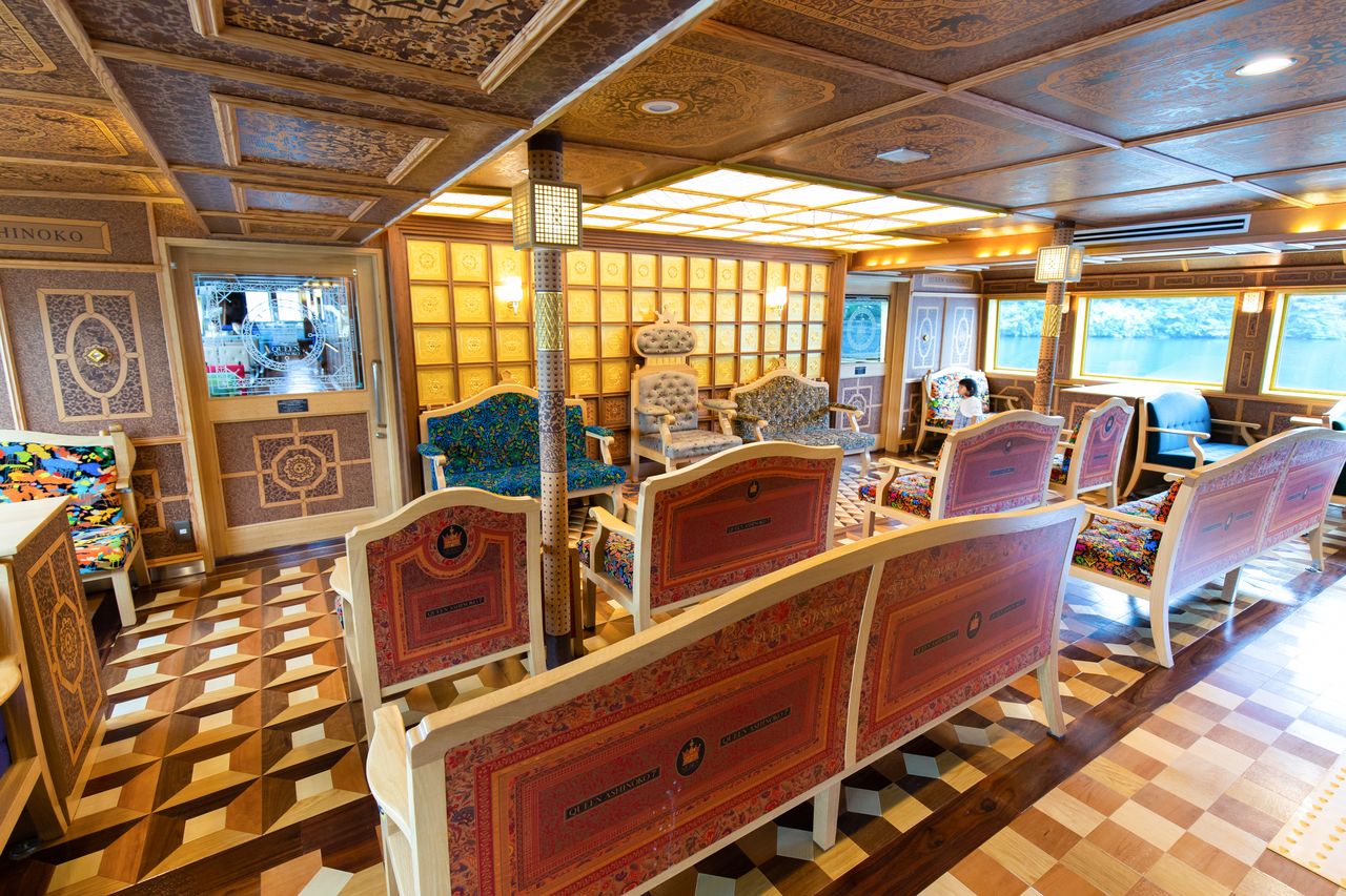 La cabine de première classe du Queen Ashinoko met à disposition de confortables canapés, depuis lesquels les passagers peuvent admirer les boiseries décoratives, le sol et son motif traditionnel de mosaïque de Hakone yosegi-zaiku ou encore les plafonds et leurs motifs recherchés.
