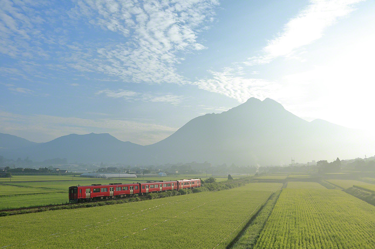 Ao&ucirc;t. Un train diesel de la s&eacute;rie KiHa 200, sur la ligne JR Ky&ucirc;dai, entre les gares de Yufuin et Minamiyufu, dans la pr&eacute;fecture d&rsquo;&Ocirc;ita. Comme la locomotive est &agrave; combustion, cela m&rsquo;a fait tr&egrave;s plaisir de pouvoir faire une photo sans les cat&eacute;naires des lignes &eacute;lectriques. La rame toute rouge ressort contre le fond du mont Yufu dans la brume matinale.