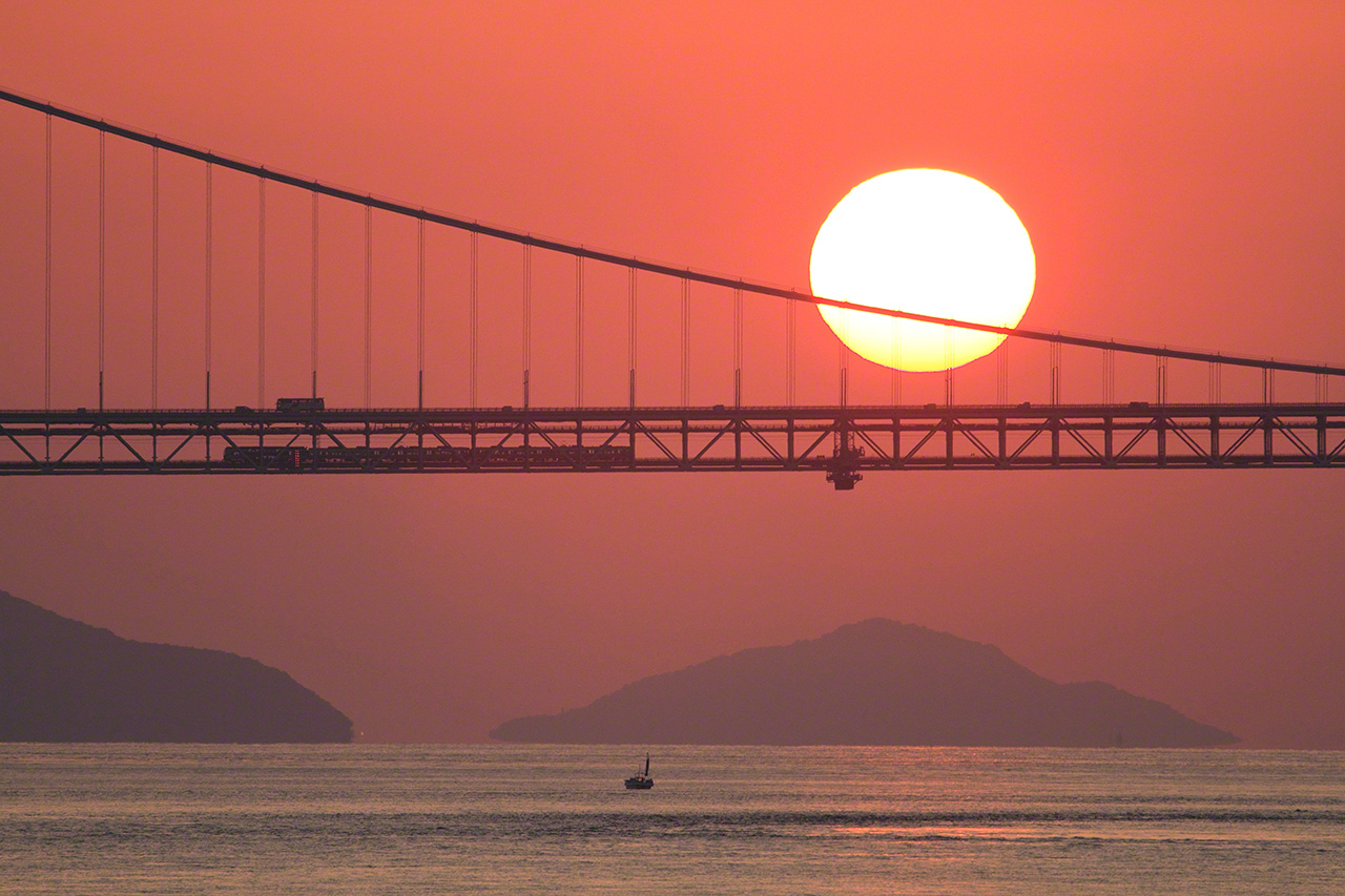 Octobre. Une rame Marine Liner, s&eacute;rie 5000, sur la ligne JR Seto &Ocirc;hashi, entre les gares de Kojima, &agrave; Kurashiki, pr&eacute;fecture d&rsquo;Okayama, et Sakaide, pr&eacute;fecture de Kagawa. Depuis l&rsquo;ouverture du pont Seto &Ocirc;hashi en 1988, le mariage entre les trains et le coucher du soleil fascine les amateurs de trains. Cette photo de la silhouette du train avec le soleil couchant en arri&egrave;re-plan a &eacute;t&eacute; faite de l&rsquo;&icirc;le de Shikoku.
