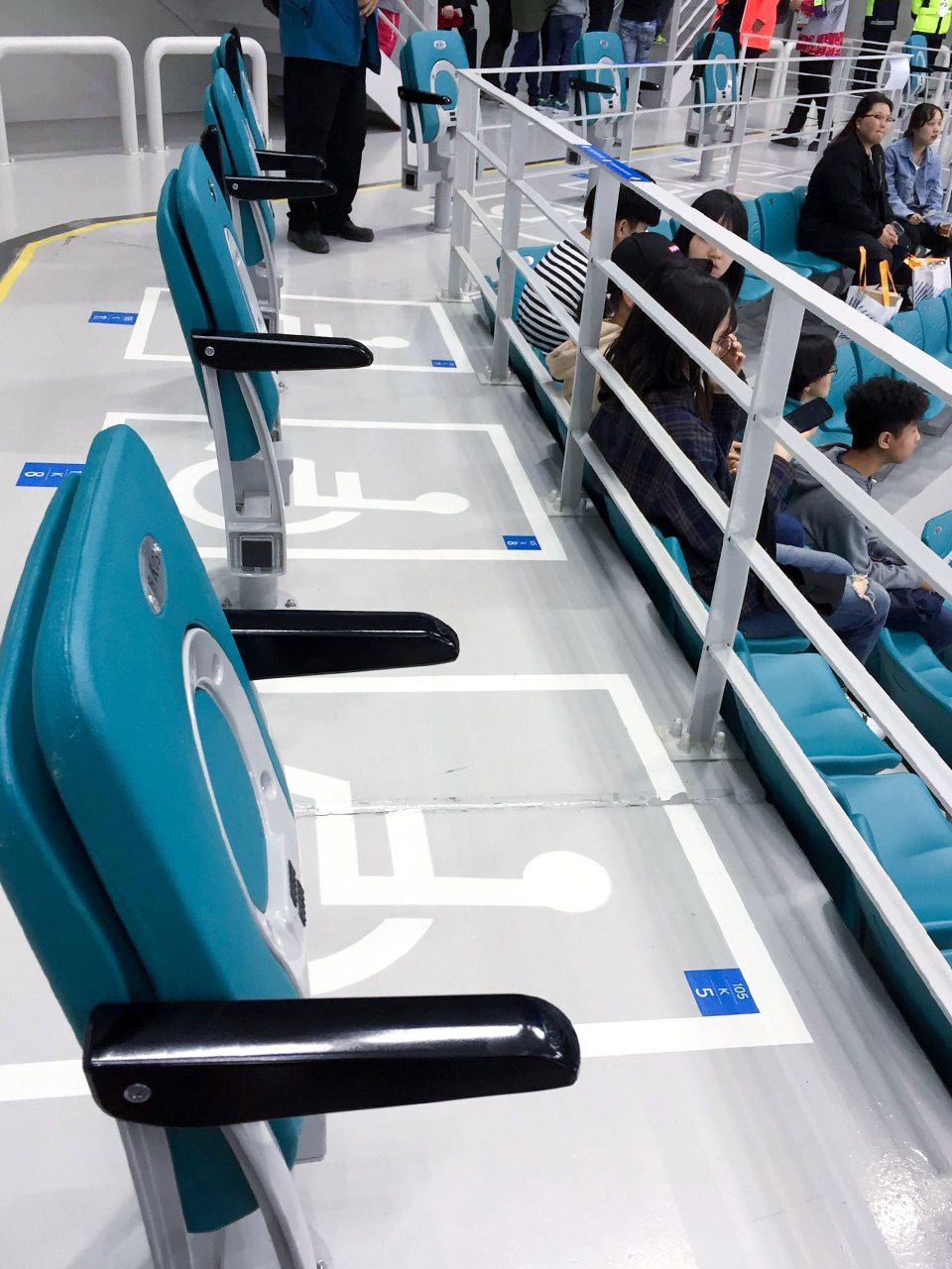 Une rangée de sièges des tribunes de la patinoire de Pyeongchang où se sont déroulées les épreuves de hockey sur luge des Jeux paralympiques de 2018.  Les emplacements pour fauteuil roulant étaient disposés d’une telle façon qu’il était impossible à deux personnes handicapées d’assister aux compétitions côte à côte.