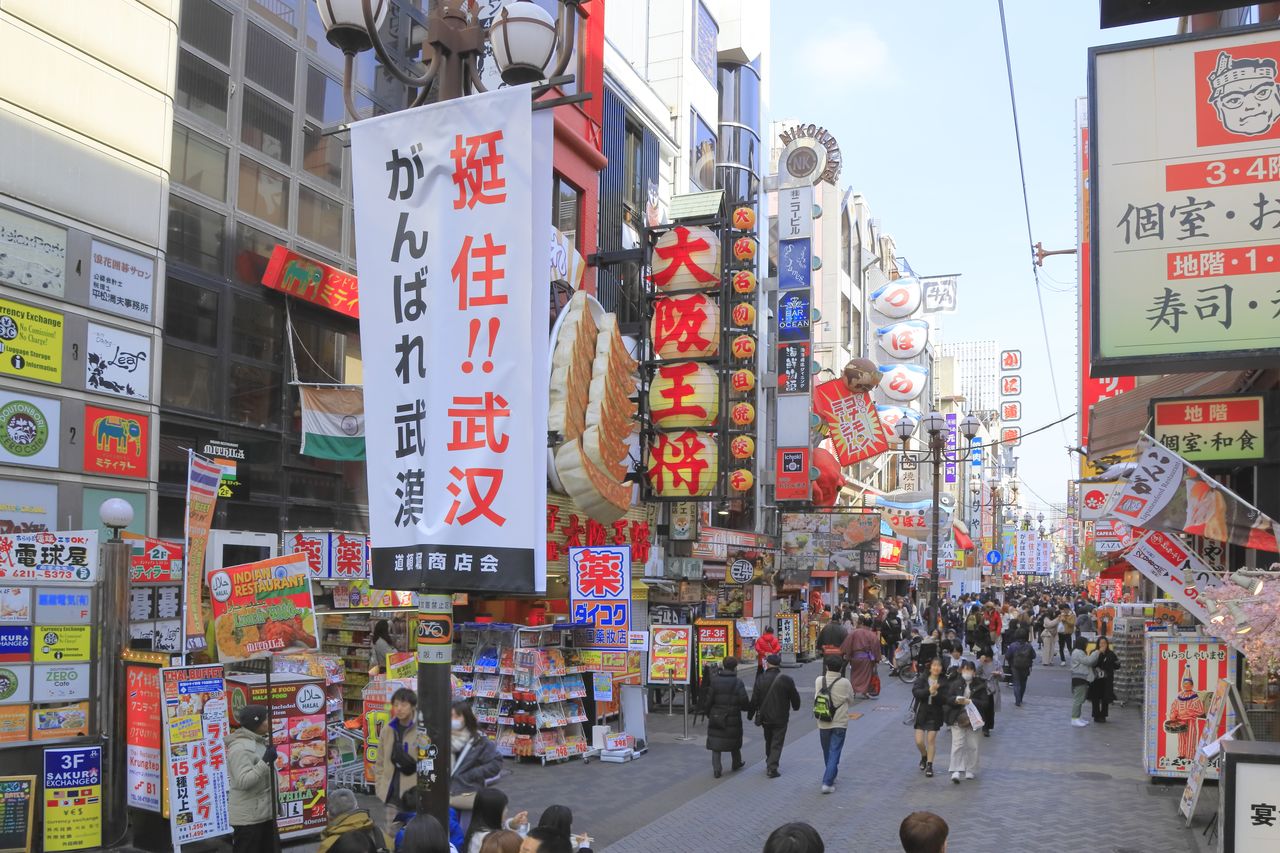 L’afflux des touristes chinois a enregistré une baisse marquée après l’éruption de l’épidémie de COVID-19. Dans le quartier de Dōtonbori, à Osaka, La bannière au premier plan porte l’inscription « Bonne chance à tous ceux qui se battent à Wuhan ! »