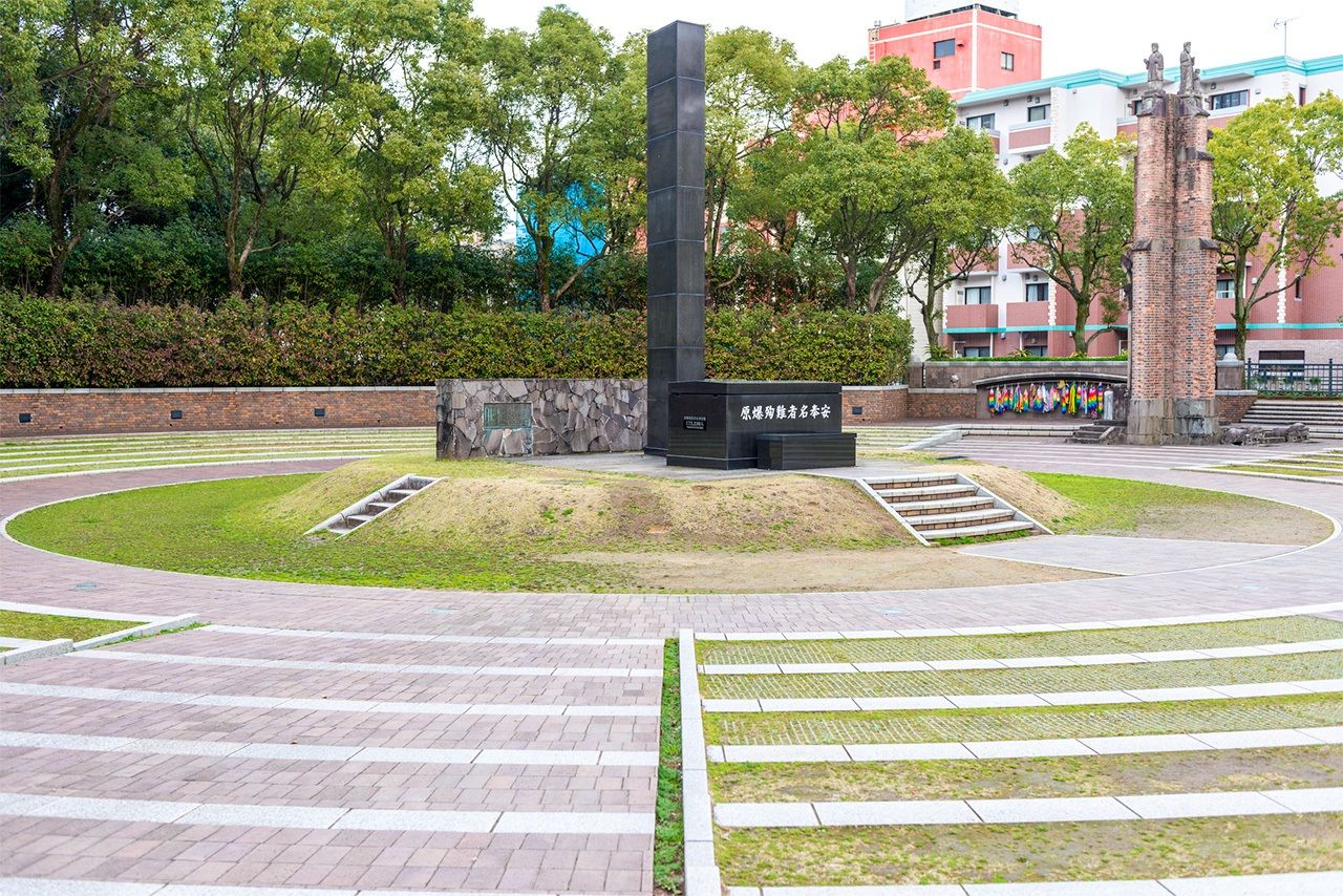 La stèle de l’hypocentre de la bombe atomique. Au fond à gauche, ce qu’il reste de l’ancienne cathédrale d’Urakami : une infime partie de son mur. (PIXTA)