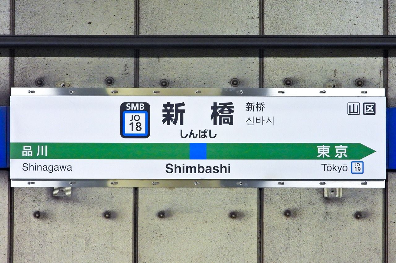 Un panneau indiquant la gare de Shimbashi illustre comment, dans le système Hepburn, le caractère hiragana ん est orthographié comme un « m » lorsqu'il précède un « b », un « m » ou un « p ». (© Pixta)
