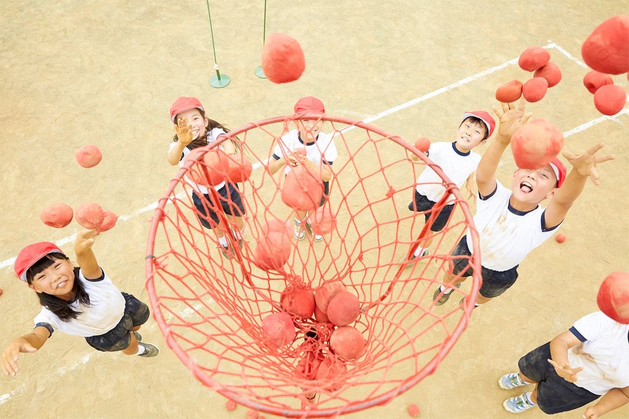 Une équipe de six enfants en train de jouer au tama-ire, qui consiste à faire entrer le plus vite possible une grande quantité de petites balles dans un panier placé au milieu d’eux.