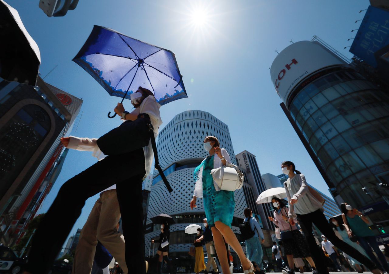 Piétons marchant avec des ombrelles sous un fort soleil. (Jiji Press)