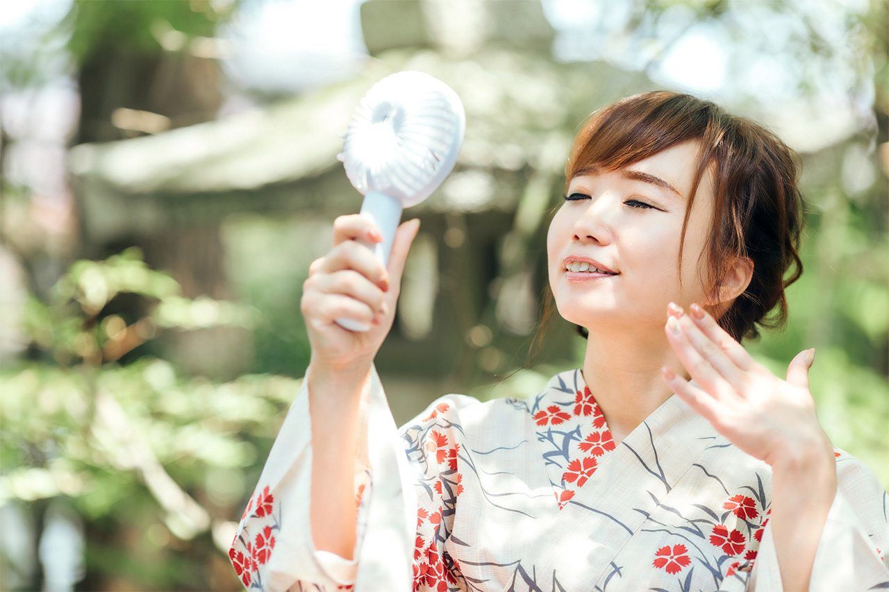 Japonaise en yukata se rafraîchissant grâce à son ventilateur électrique portatif. (© Pixta)
