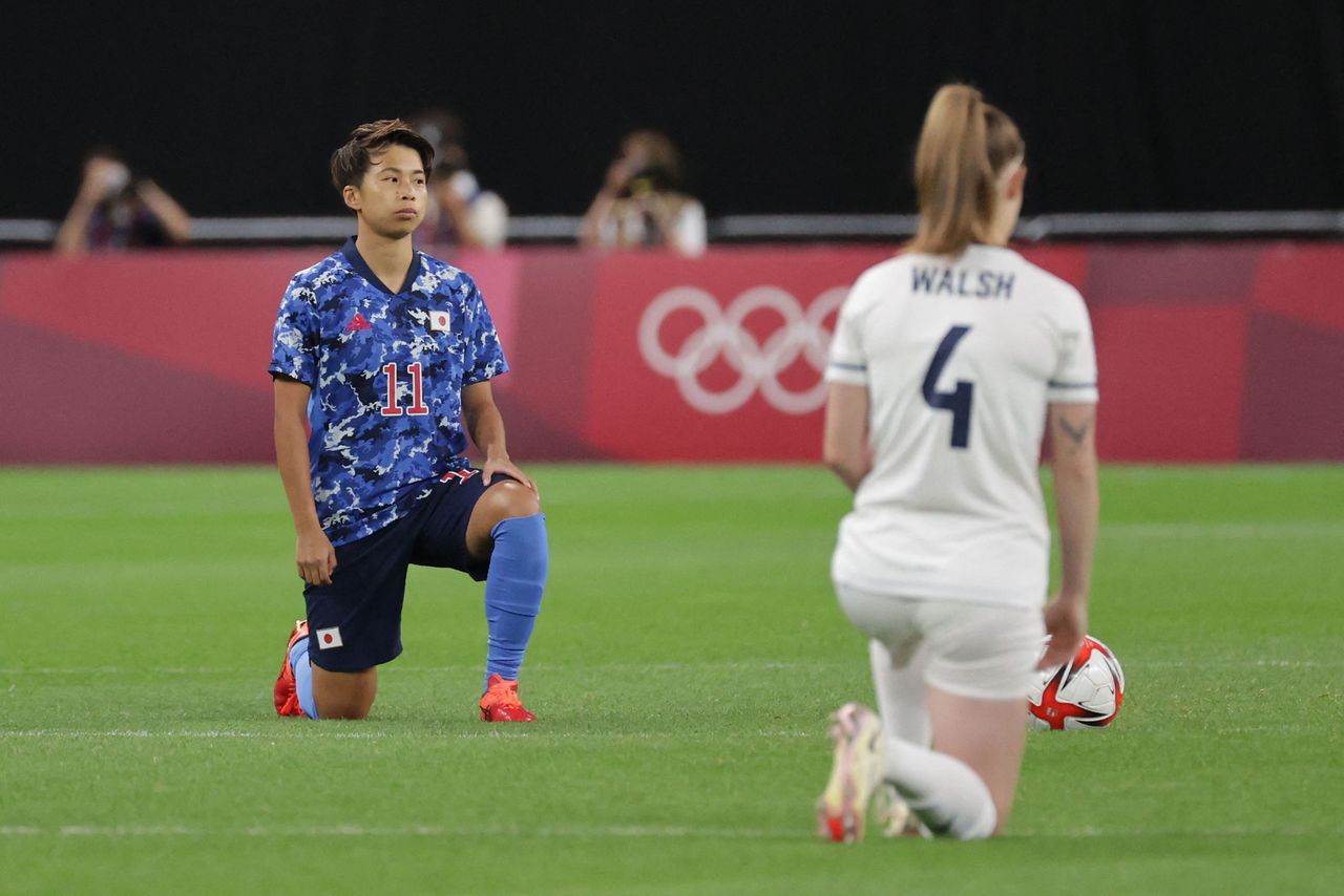 Tanaka Minami (à gauche), membre de l'équipe nationale féminine de football du Japon, et une joueuse britannique mettent un genou en terre pour protester contre le racisme avant un match au Sapporo Dome, Hokkaidô, le 24 juillet 2021. (AFP/Jiji)